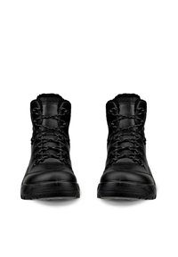 Paar schwarze High-Top-Stiefel mit dicken Sohlen und gemusterten Schnürsenkeln, von vorne auf weißem Hintergrund gesehen.