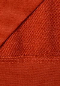 Tessuto di cotone rosso con due texture: una maglia liscia e un motivo tessuto leggermente in rilievo, con cuciture visibili lungo il bordo inferiore.