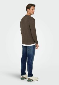 Brun genser med lange ermer og rund hals, kombinert med bl�å jeans og hvite joggesko med grønne og grå detaljer.