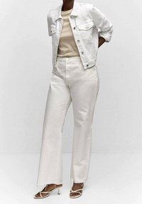 Giacca in denim bianco sovrapposta a un top beige, abbinata a pantaloni bianchi a gamba larga. Dettagli notevoli includono orli sfrangiati e tacchi con cinturini.