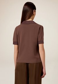 Brun kortærmet top med en kontrasterende glitrende krave og manchetter. Glat tekstur, tætsiddende design og en afslappet silhuet.