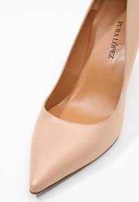Escarpin en cuir nude à talon haut, bout pointu, texture lisse et léger éclat. Intérieur avec une semelle intérieure beige clair.