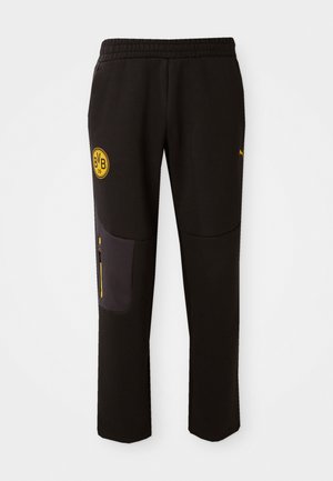 Pantaloni sportivi neri con vita elastica, caratterizzati da un logo circolare giallo e una tasca con zip in un pannello grigio scuro a contrasto.