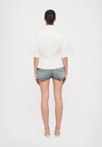 Witte, gestructureerde blouse met korte, opbollende mouwen en een rugpasdetail, gecombineerd met versleten denim shorts. Soepele textuur, moderne snit.