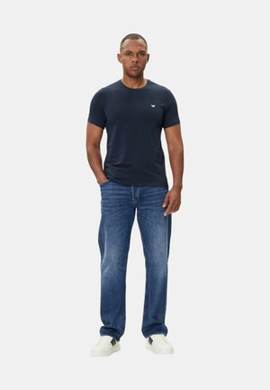 Marineblå t-shirt med rund hals i en tætsiddende design, parret med lyseblå denimjeans og hvide sneakers. Hvidt logo på tshirtens bryst.