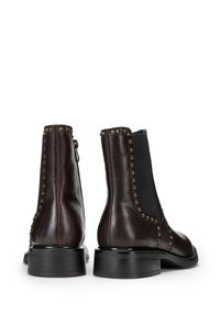 Brązowe skórzane botki sięgające kostki z elastycznymi panelami bocznymi, wypukłymi dodatkami wzdłuż szwów oraz płaską czarną podeszwą. Gładka faktura i elegancki kształt.