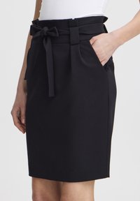 Jupe noire avec une taille cintrée, poches latérales et une ceinture à nouer. Fabriquée dans un tissu lisse avec une silhouette structurée.