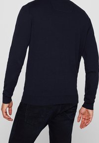 Pull tricoté bleu marine avec texture côtelée, encolure ronde et poignets ajustés. Vue de dos montrant un détail de couture subtil. Associé à un jean foncé.