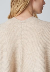 Pull en tricot couleur crème avec une texture côtelée, doté d'un col rond et d'une couture dans le dos. Matière douce et légère.
