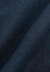 Țesătură din in de culoare albastră închisă, cu o suprafață texturată, care pune în evidență subtilități neregulate și cute ce indică finețea și fluiditatea.