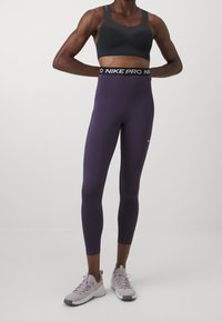 Schwarzer Sport-BH aus strukturiertem Stoff, lila Leggings mit einem Nike Pro Taillenbund und helllila Sportschuhen. Glattes und enganliegendes Design.