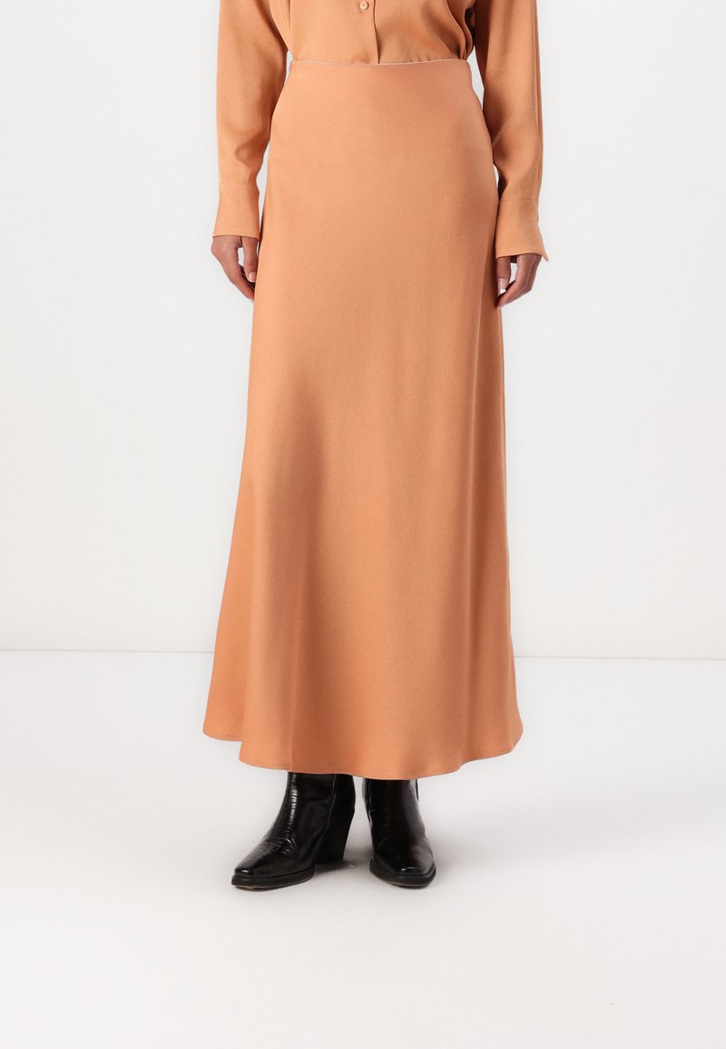 Dlhá, priliehavá sukňa v jemnej broskyňovej farbe, vyrobená z hladkej látky. Má rovný strih a siahne po členky.