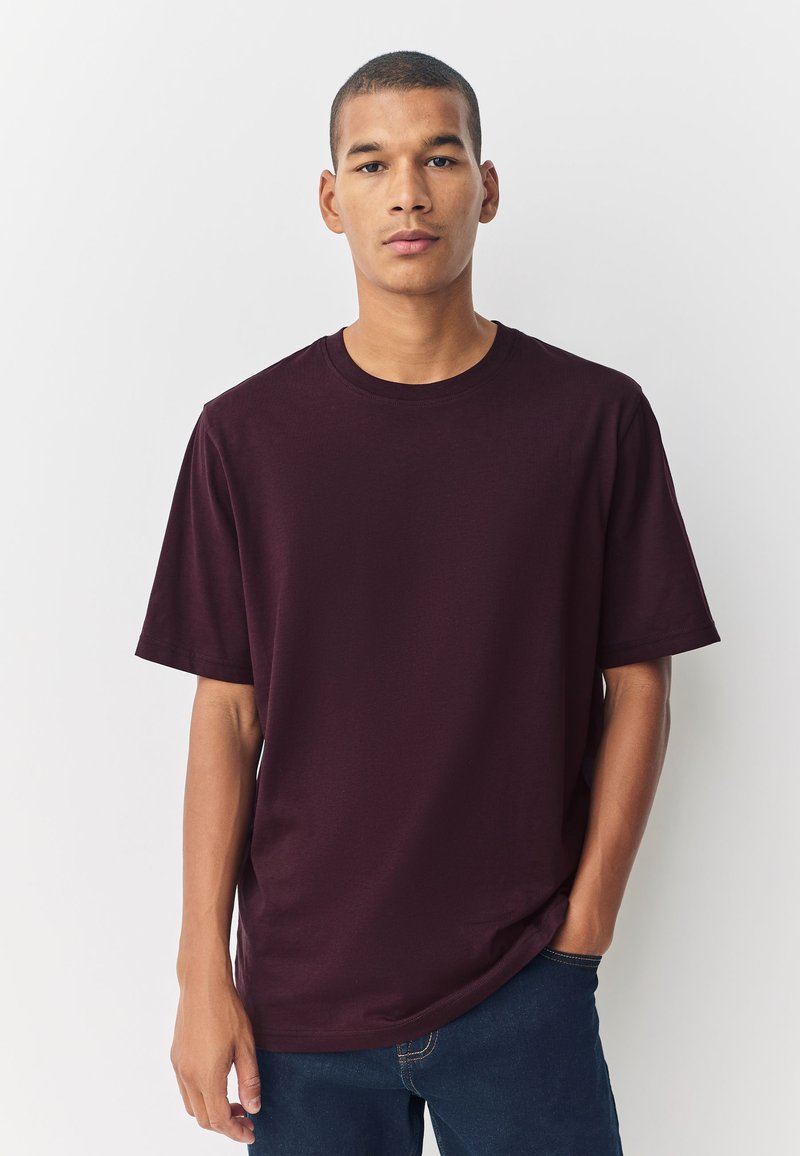 T-shirt di cotone color bordeaux con scollo rotondo e maniche corte, indossata da una persona, su uno sfondo neutro.