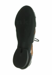 Semelle de chaussure noire avec surface en caoutchouc texturé, dotée d'une découpe centrale et d'un marquage. La partie supérieure présente un accent en cuir marron sur les côtés.