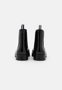 Bottines en cuir verni noir avec une semelle épaisse et des boucles de maintien, dotées d'une finition lisse et de détails de couture sur les côtés.