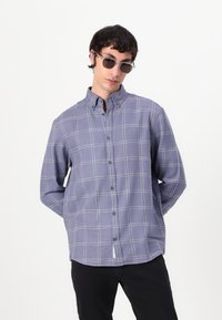 Camicia a maniche lunghe con bottoni di colore viola chiaro e motivo plaid, con colletto a punta e orlo arrotondato, abbinata a pantaloni neri.