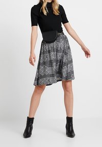 Svart kortärmad topp som matchas med en knälång mönstrad kjol i svart och vitt. Outfiten inkluderar en svart bältesväska och ankelstövlar.