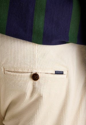 Cremfarbige Cordhosen mit strukturiertem Finish und einem braunen Knopfakzent, ausgestattet mit einem kleinen blauen "JOULES"-Label in der Nähe der Gesäßtasche.
