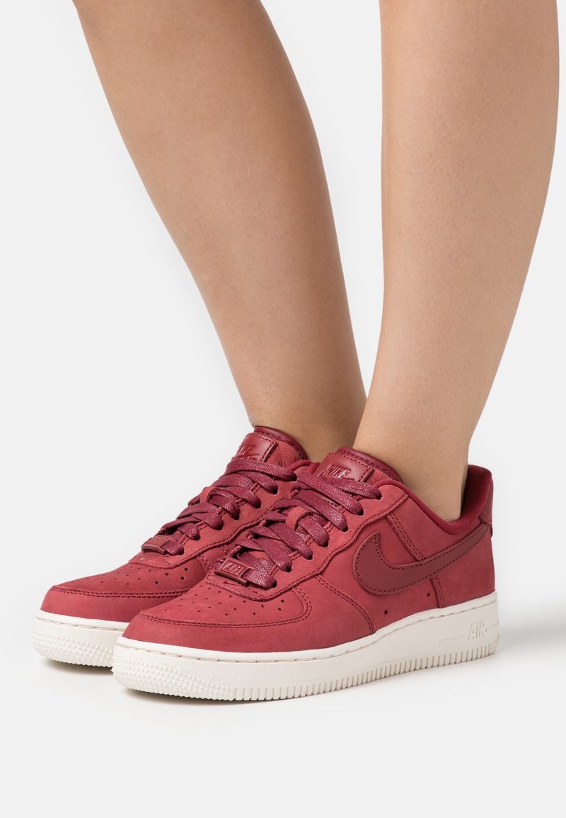 Baskets Nike Air Force 1 en cuir rouge avec boîtier à orteils perforé, lacets plats et semelle en caoutchouc blanche. Accentué par le logo Swoosh emblématique.