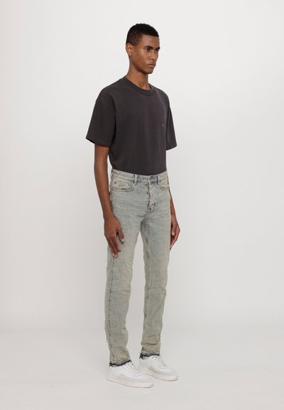 Męska ciemnoszara, luźna koszulka, jasnoniebieskie dopasowane dżinsy i białe trampki. Koszulka ma okrągły dekolt; dżinsy mają subtelne przetarcia.