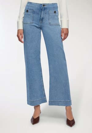 Jeans in denim azzurro chiaro a gamba larga con vita alta, due tasche frontali e dettagli di cucitura in evidenza. Abbinati a scarpe marroni a punta.