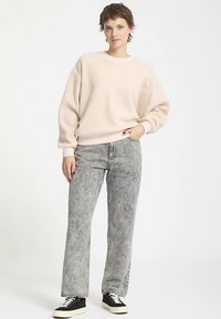 Felpa beige chiaro oversize, jeans grigi acid-wash a gamba dritta e sneakers nere. Outfit casual con design minimalista e texture morbide.