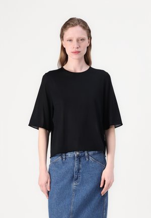 Top nero a maniche corte con vestibilità ampia e scollatura rotonda, realizzato in tessuto morbido, abbinato a una gonna di jeans a vita alta.