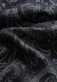 Tissu foncé avec des motifs paisley en relief complexes dans des tons de noir et de gris, montrant la texture et les plis.