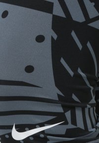 Szary i czarny materiał sportowy z wyraźnymi geometrycznymi wzorami, gładką fakturą i białym logo Nike na dole.