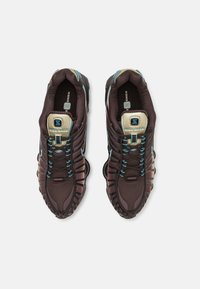 Dark brown athletic shoes with a textured upper, turquoise laces, and a prominent sole design featuring unique cushioning elements.