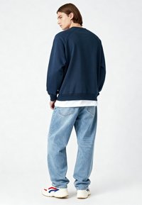 Sweat-shirt bleu marine avec poignets et ourlet côtelés, associé à un jean ample bleu clair et des baskets blanches avec des accents rouges et bleus.