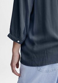 Marineblauwe textuur shirt met opgerolde mouwen en een knoopdetail; aansluitend ontwerp met een iets losse pasvorm.