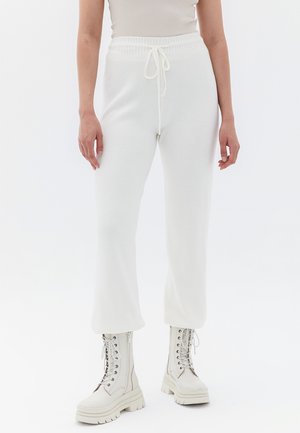 Pantalons de jogging blancs à côtes avec taille élastique et cordon de serrage. Associés à des bottes blanches à lacets avec semelles épaisses.
