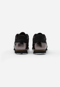 Tênis pretos com um calcanhar texturizado em preto, detalhes em bronze escuro brilhante e uma sola branca com manchas. Design minimalista com colarinho acolchoado.