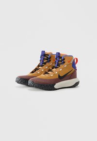Magas szárú Nike sportcipők barna, burgundi és kék színben, fekete talppal, fekete és lila fűzővel, valamint piros logó kiemelésekkel.