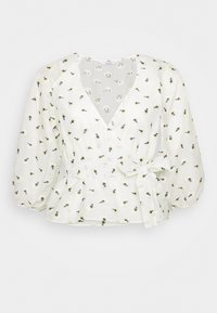 Blouse blanche avec peplum, col en V, manches bouffantes et taille à nouer. Présente une broderie florale en noir et jaune sur un tissu léger.