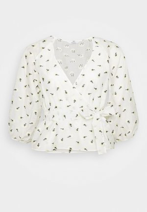 Blouse blanche avec peplum, col en V, manches bouffantes et taille à nouer. Présente une broderie florale en noir et jaune sur un tissu léger.