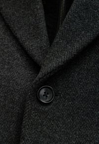 Abrigo de lana gris oscuro con un cuello de muesca y un botón redondo negro con cuatro agujeros. La tela tiene un acabado texturizado.