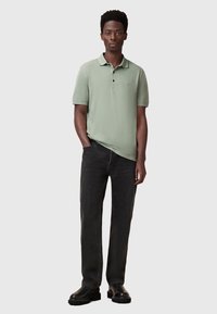 Ljusgrön polo-shirt med krage, svarta jeans och svarta stövlar. Enkelt mönster med korta ärmar och subtil logotyp på bröstet.