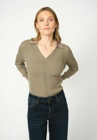 Pulover ribbed, de culoare verde măsliniu, cu decolteu în V și guler taupe; design ajustat cu mâneci lungi. Asortat cu blugi de culoare albastru închis.