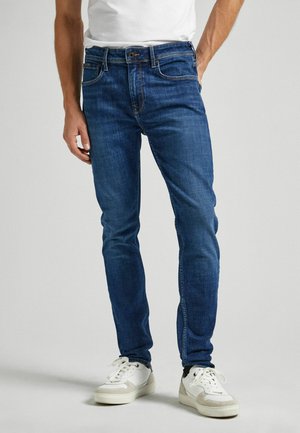 Jean en denim bleu à coupe slim avec une taille mi-haute, comportant cinq poches, des coutures contrastées et une fermeture à zip.