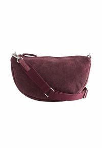 Bordeaux ruskind skuldertaske med en buet form, sølvhardware og en bred stofrem. Glat tekstur, lynlåslukning øverst.