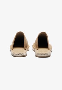 Beige espadriller med åpen bak, laget av semsket skinn, med en flat såle som har et vevd jute-detalj rundt kanten.