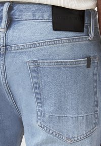 Jeans in denim azzurro chiaro con un taglio a vita media, dotati di un'etichetta in pelle nera in vita e tasche posteriori con dettagli di cucitura sottili.