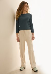 Haut à manches longues teal associé à un pantalon beige avec cordon de serrage. L'ensemble présente une coupe décontractée et un tissu léger et doux avec des textures subtiles.