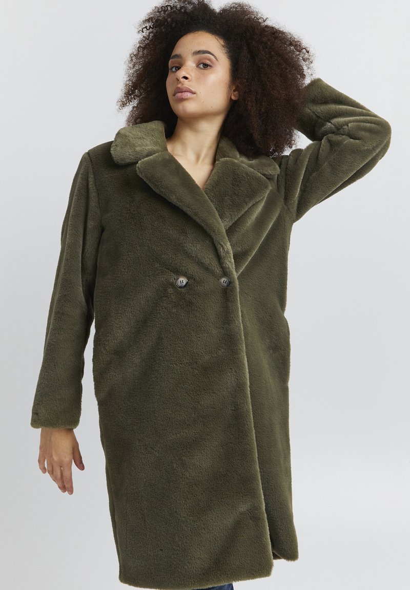 Faux fur olivengrøn frakke med dobbeltknaplukning, stor klapkrave og sidelommer, der fremviser et blødt, tekstureret stof.