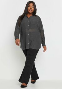 Zwarte button-up shirt met een gestructureerd design, lange mouwen en een kraag, gecombineerd met zwarte flare broeken en zwarte schoenen.