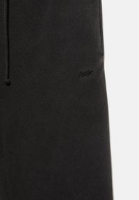 Čierne tepláky vyrobené z mäkkej, textúrovanej tkaniny. Disponujú pásom na šnurovanie a vyšitým logom na boku. Jednoduchý a ležérny dizajn.