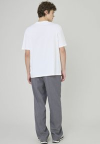 T-shirt en coton blanc à manches courtes, coupe décontractée ; associé à un pantalon droit texturé gris et des baskets noir et blanc.