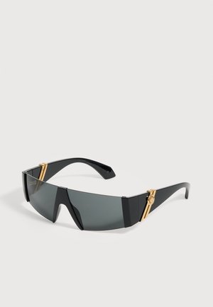 Lunettes de soleil enveloppantes noires avec verres teintés foncés et accents décoratifs dorés sur les branches.